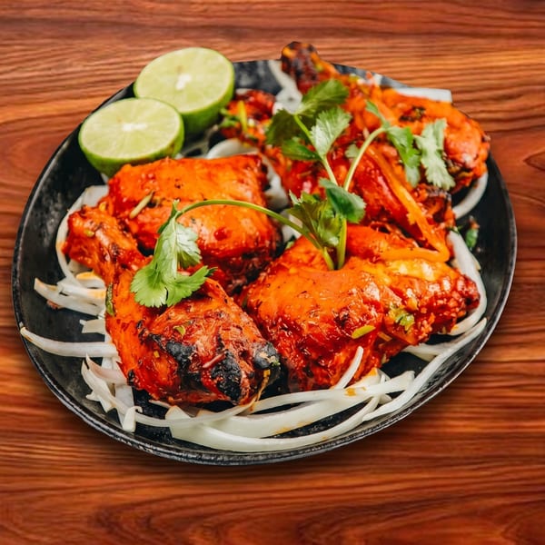 Tandoori chicken pieces with cilantro and lime wedges on a bed of sliced onions.