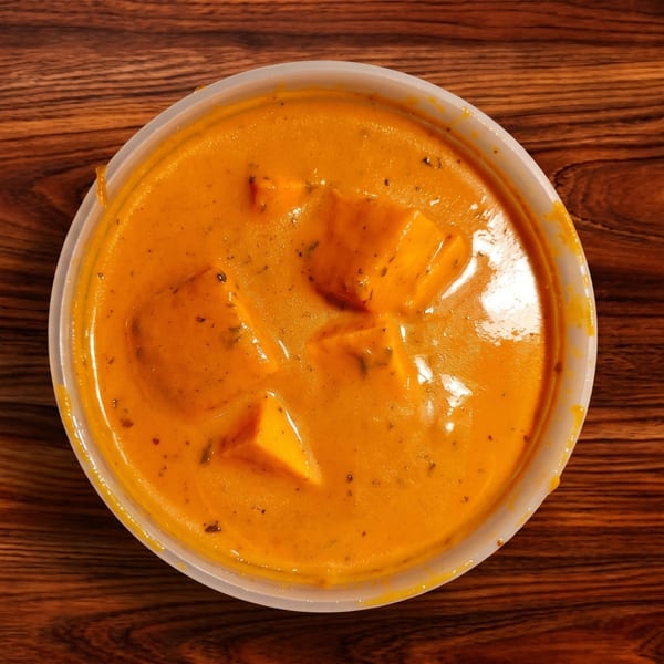 Overhead view of paneer butter masala in a white plastic container on a wooden table.