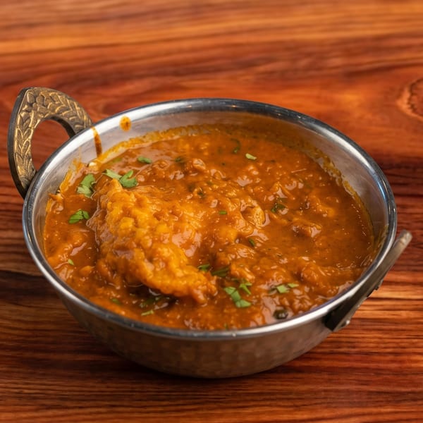 A metal bowl filled with a rich orange curry, garnished with fresh green herbs, on a wooden table.