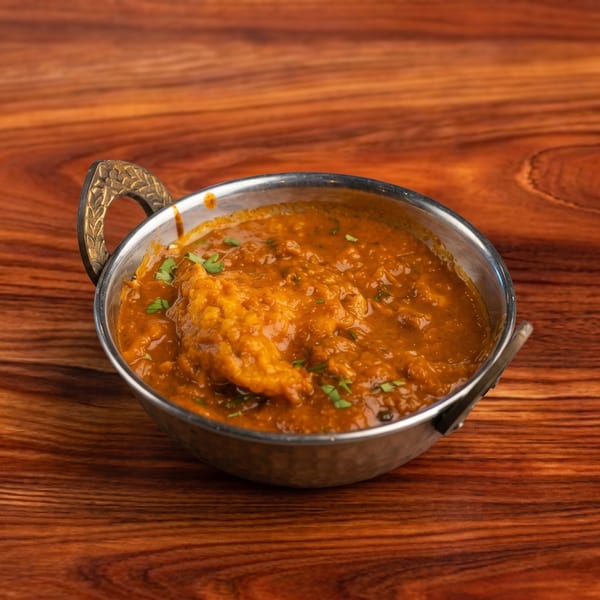 A metal karahi bowl filled with a rich, orange-brown curry, garnished with fresh green herbs.