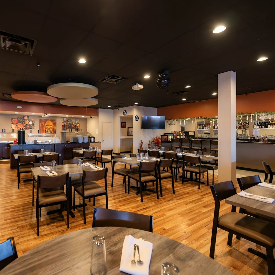 Spacious restaurant dining room with wooden floors, set tables, a buffet, and a bar area.
