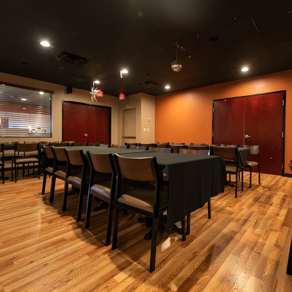 A private dining room with long tables draped in black cloths and chairs on a wooden floor.
