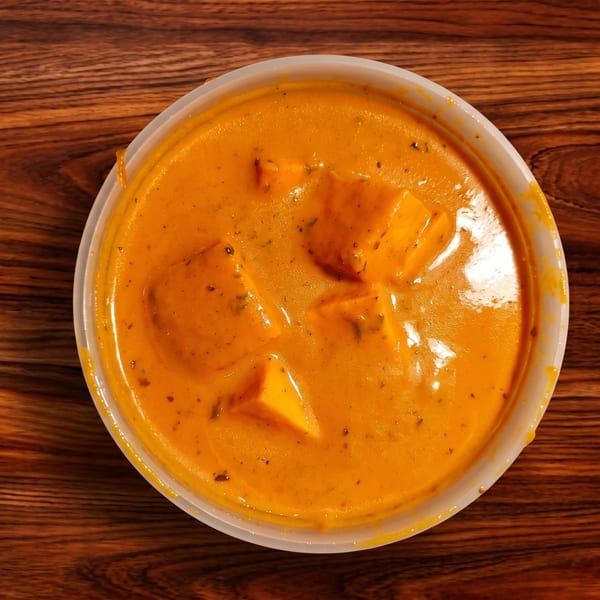 Overhead view of paneer butter masala in a white plastic container on a wooden table.
