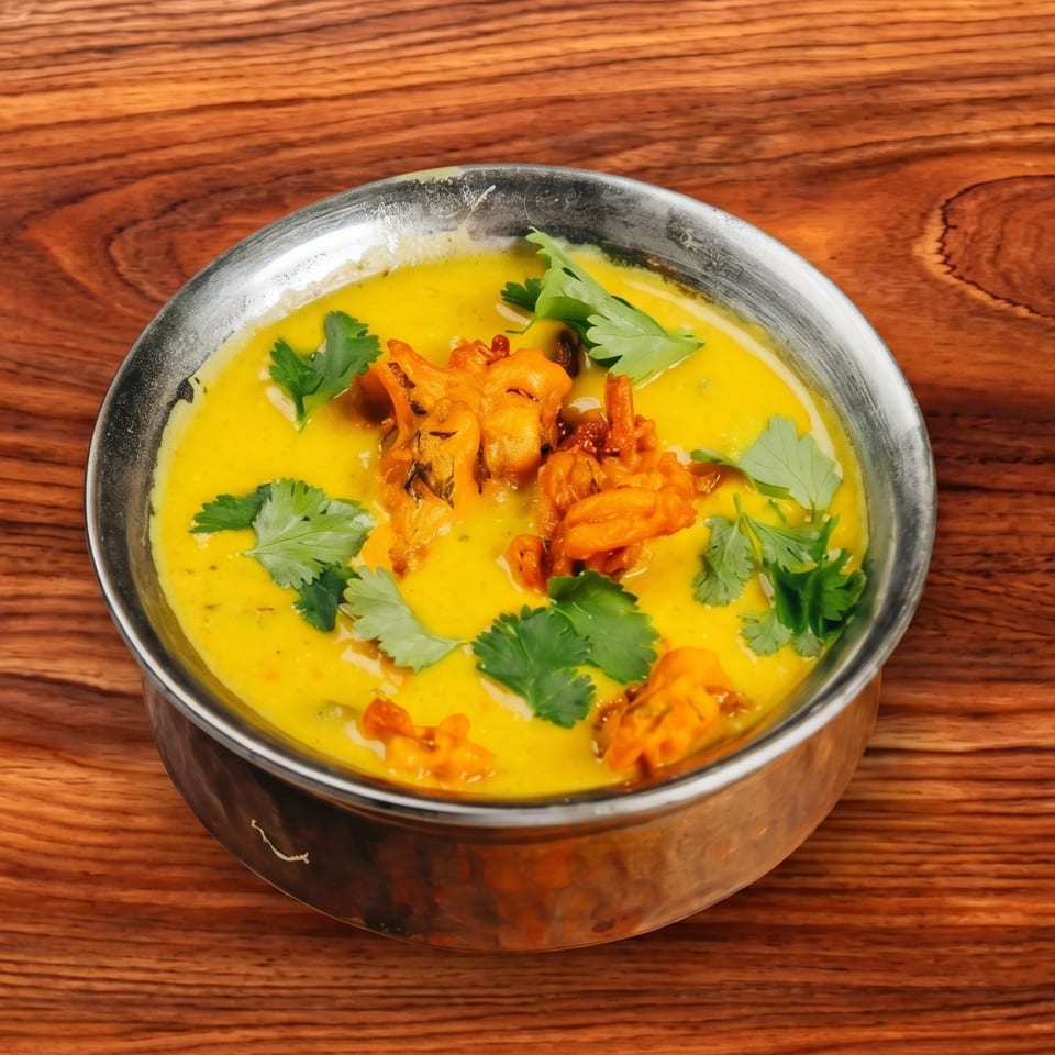 A metal bowl filled with yellow curry, topped with fried fritters and fresh cilantro.