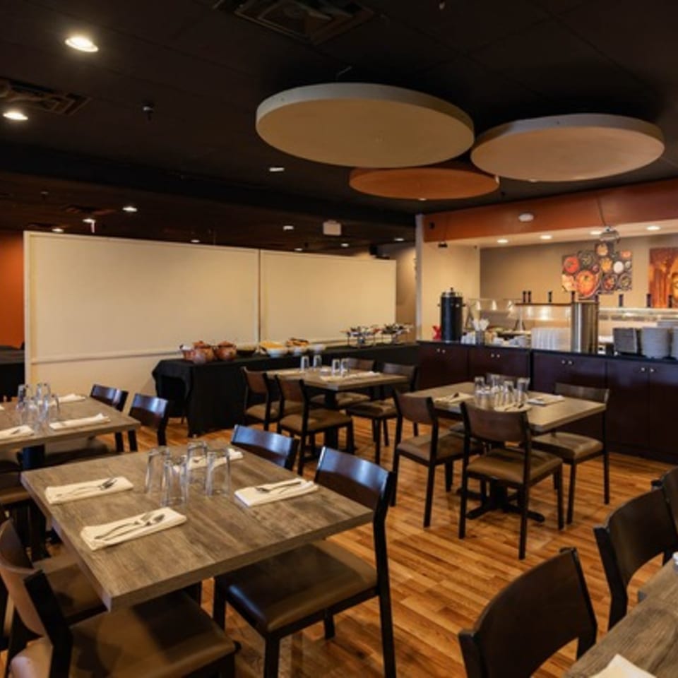 A restaurant dining room with set tables, a buffet line, and modern circular ceiling panels.